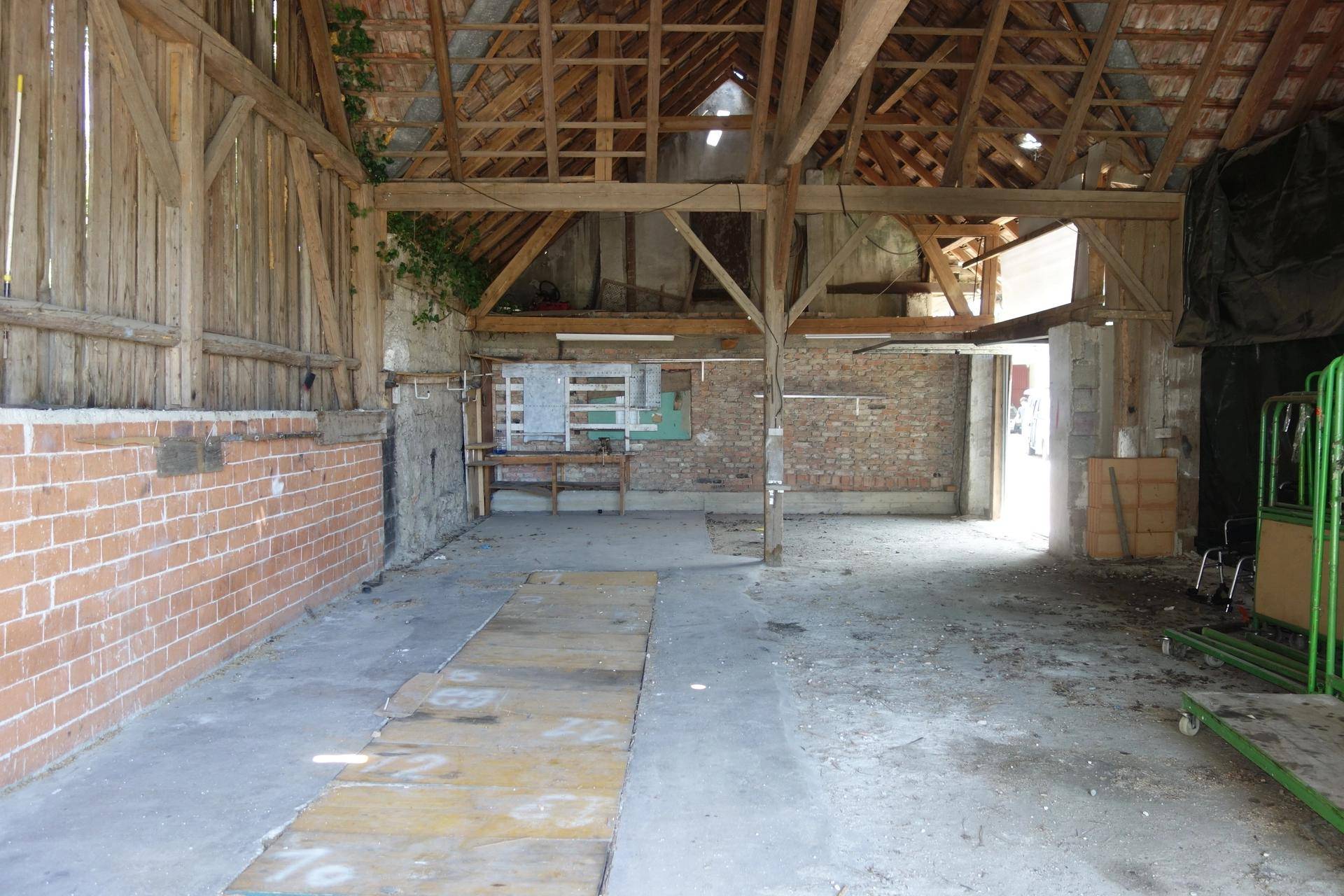 Großer, leerer Scheunenraum mit sichtbaren Holzbalken und Ziegelwänden, bereit zur Renovierung.