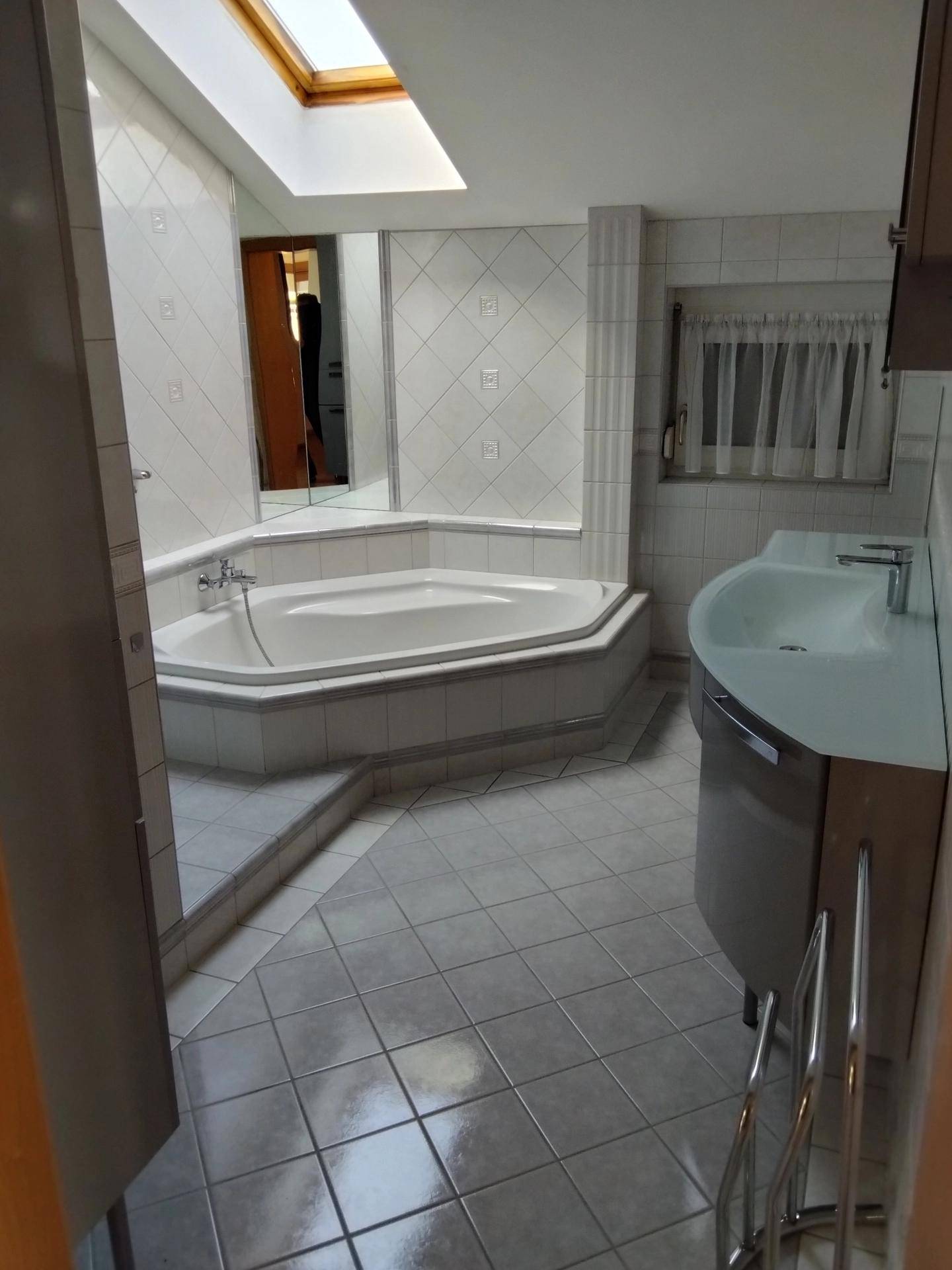 Badezimmer mit Eckbadewanne, Dachfenster und weißen Fliesen.