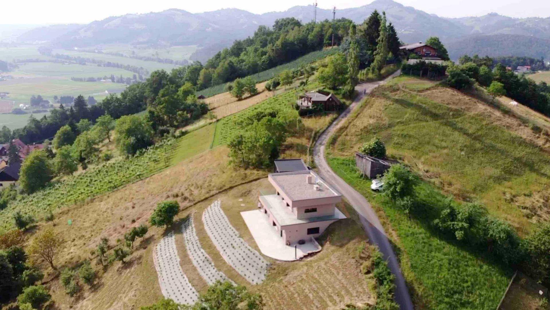 Panoramablick aus der Vogelperspektive auf ein modernes Haus in einer weitläufigen, grünen Hügellandschaft.