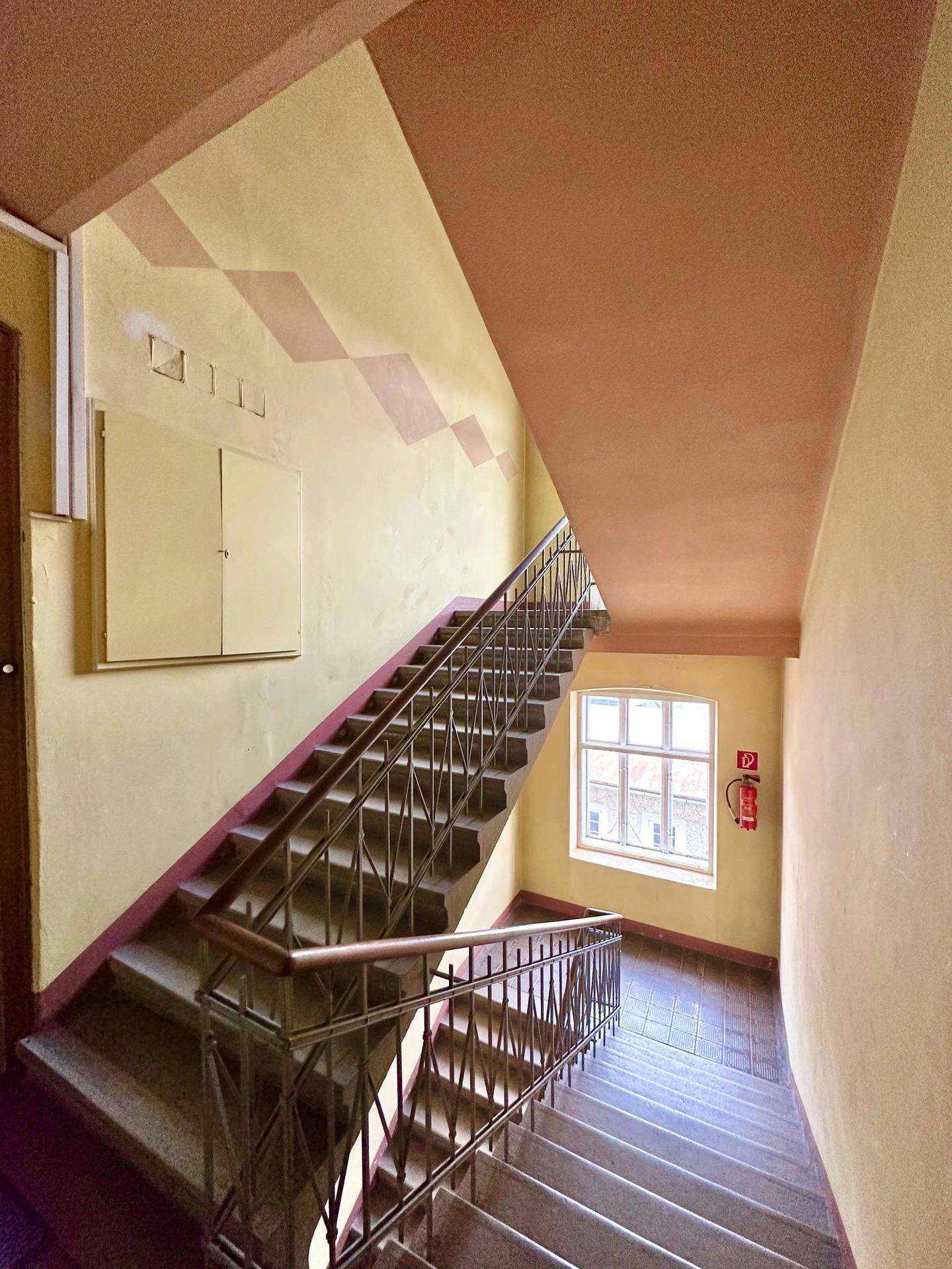 Historisches Treppenhaus mit Steinstufen, Metallgeländer und farbigen Wänden.