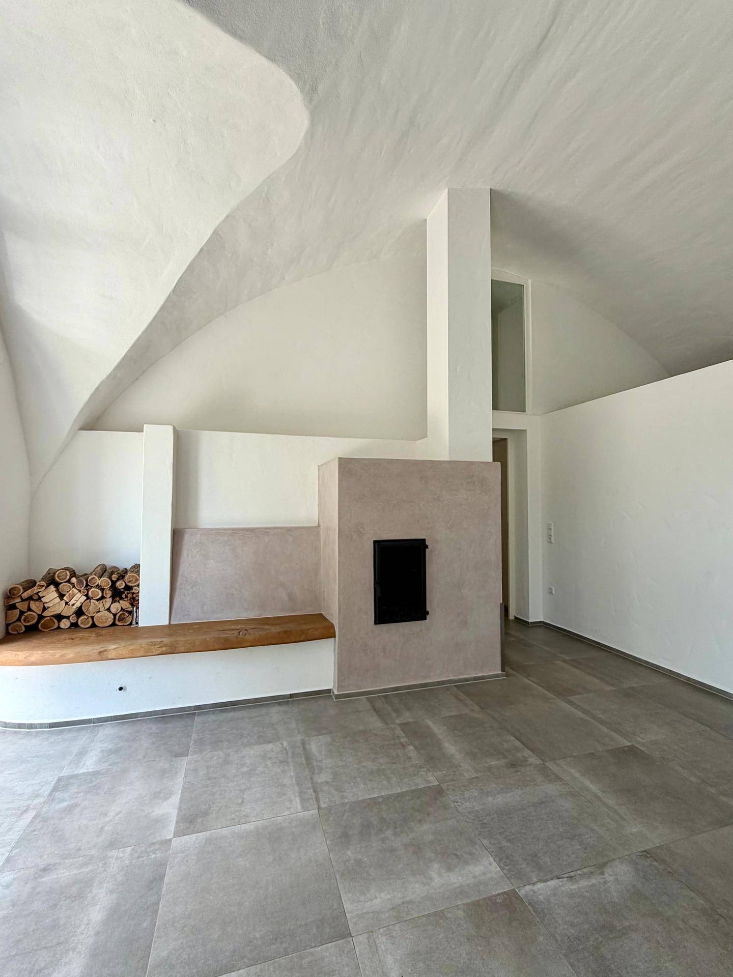 Geräumiger Wohnbereich mit modernem Kamin, Holzablage und beeindruckender Gewölbedecke.
