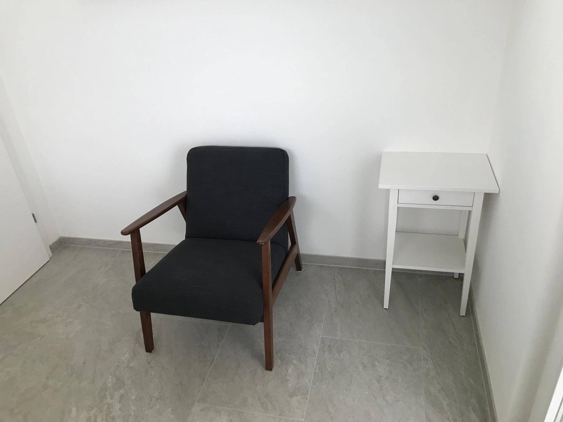 Einfacher Innenraum mit einem Sessel und einem kleinen Beistelltisch auf Fliesenboden.