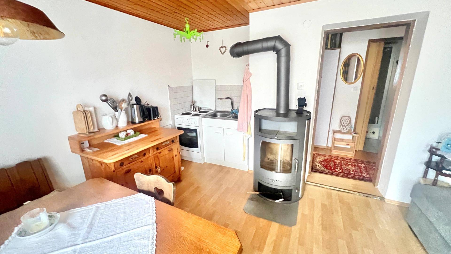 Offener Wohn- und Essbereich mit kleiner Küche, Holzdecke und einem Holzofen.