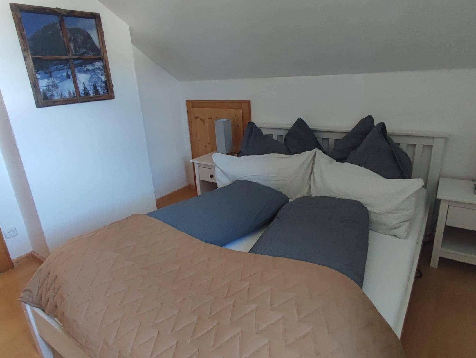 Helles Schlafzimmer mit Doppelbett und dekorativem Bergbild an der Wand.