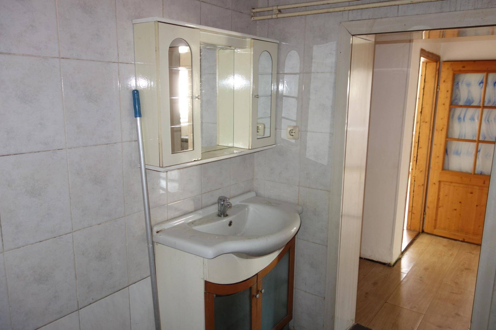 Badezimmer mit gefliesten Wänden und Boden, einem Waschbecken mit Unterschrank und Spiegelschrank.