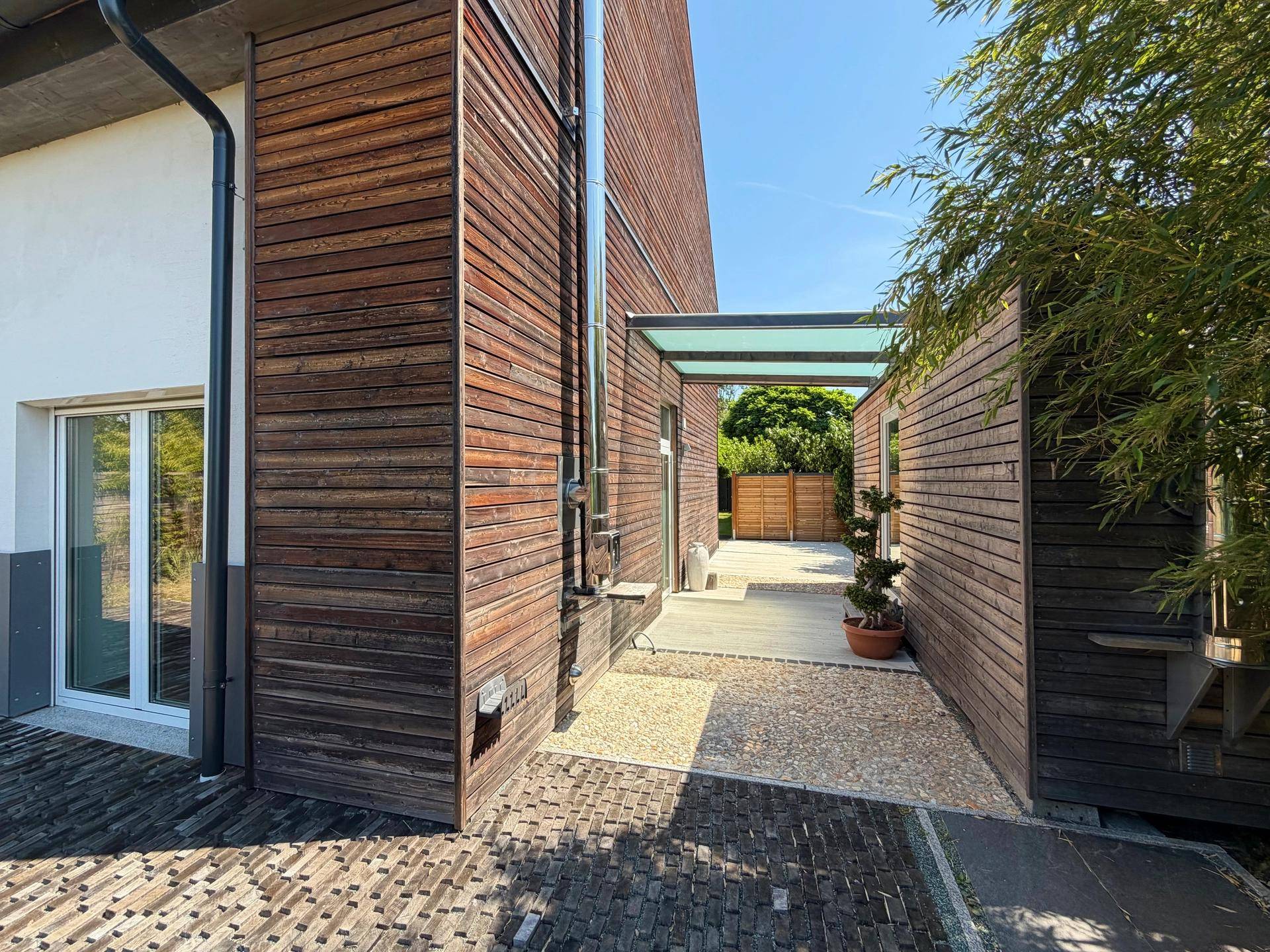 Moderne Holzfassade des Gebäudes mit einem überdachten Gang und Bambuspflanzen.
