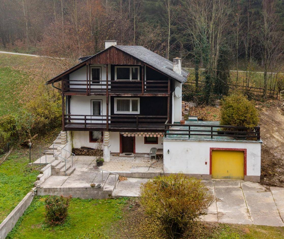 Haus mit mehreren Balkonen und einer Garage, umgeben von einer grünen Landschaft.
