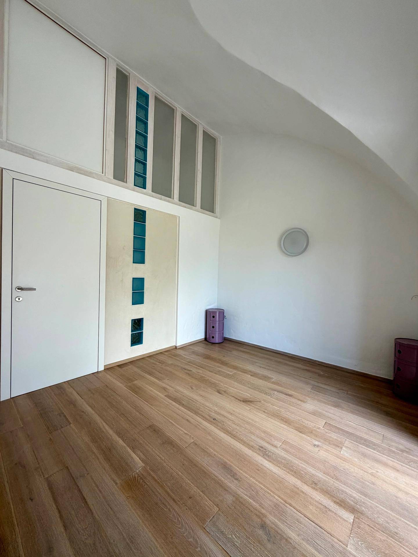 Geräumiges Zimmer mit Holzboden, Gewölbedecke und dekorativen Glasbausteinen.