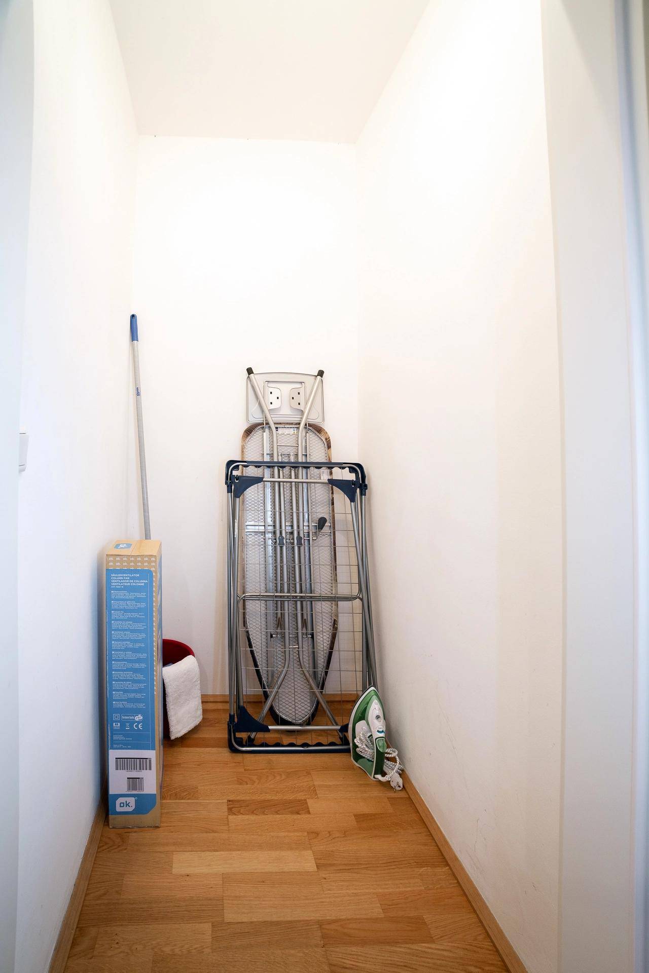 Praktischer Abstellraum mit Bügelbrett, Bügeleisen und Reinigungsutensilien.