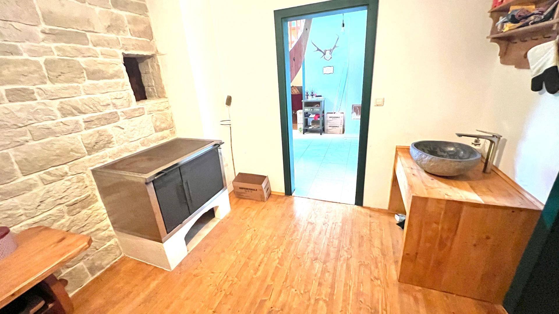 Traditionelle Küchenzeile mit Steinwaschbecken und Holzmöbeln, ergänzt durch einen Holzofen.