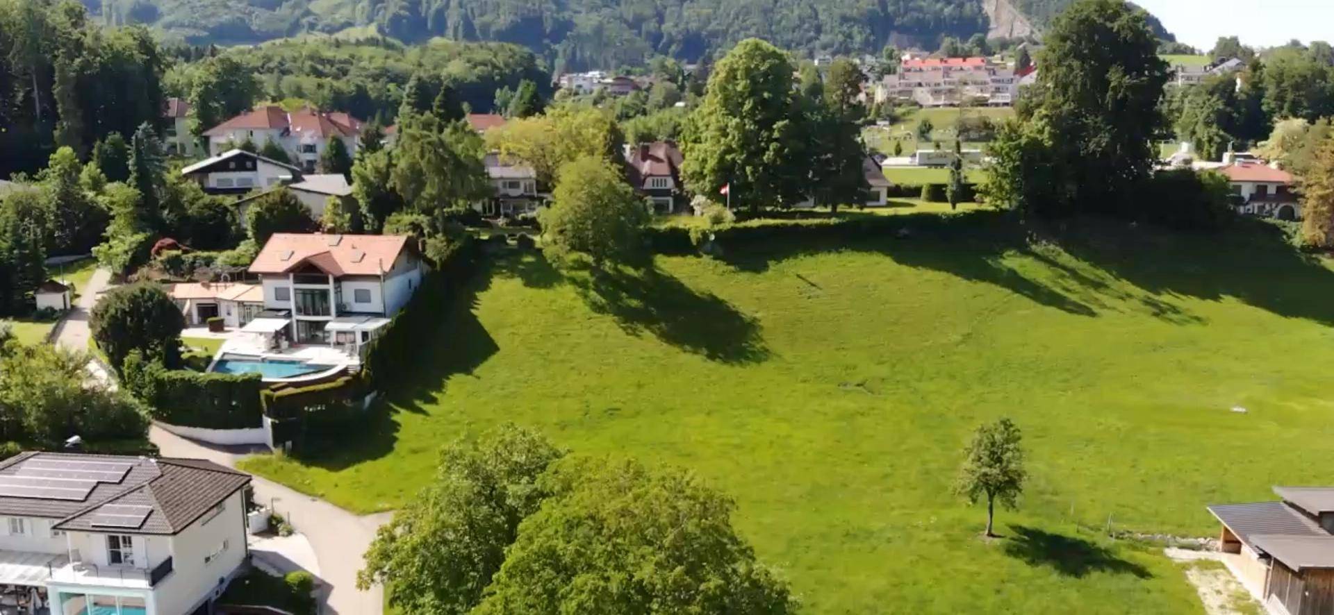 Weitläufige Wohngegend mit grünen Hügeln und vereinzelten Häusern unter klarem Himmel.