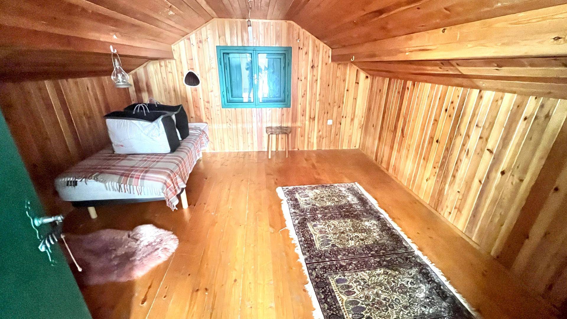 Gemütliches Schlafzimmer im Dachgeschoss mit Holzwänden, Holzboden und einem kleinen Fenster.