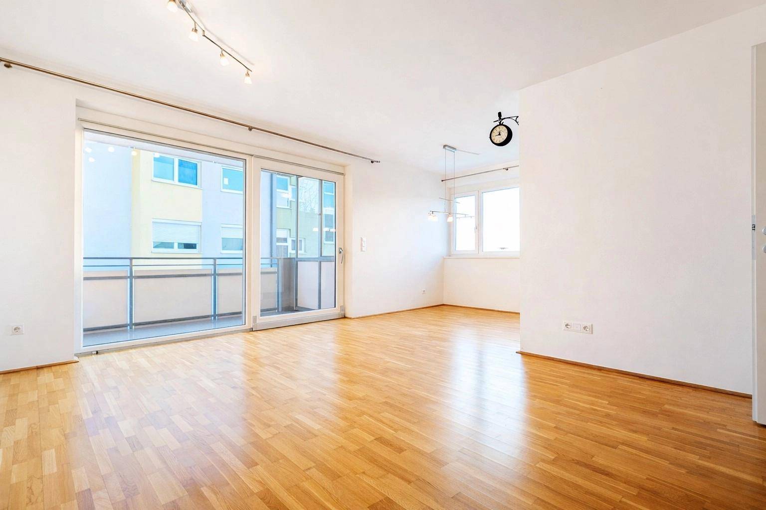 Lichtdurchflutetes Wohnzimmer mit Holzboden und Zugang zu einem Balkon, bietet viel Tageslicht.