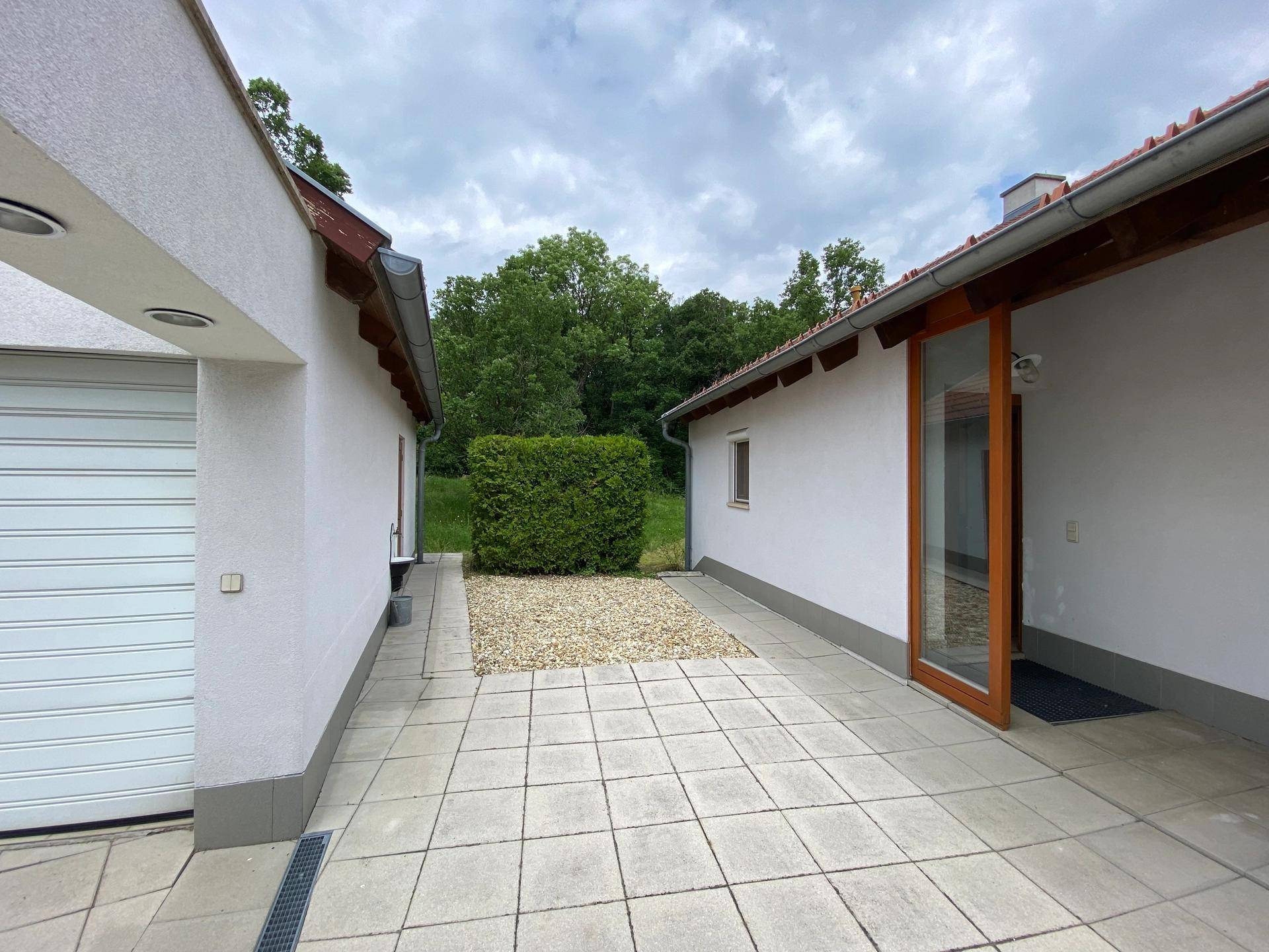 Gepflasterter Weg zwischen Garage und Haus, mit einer Hecke im Hintergrund.