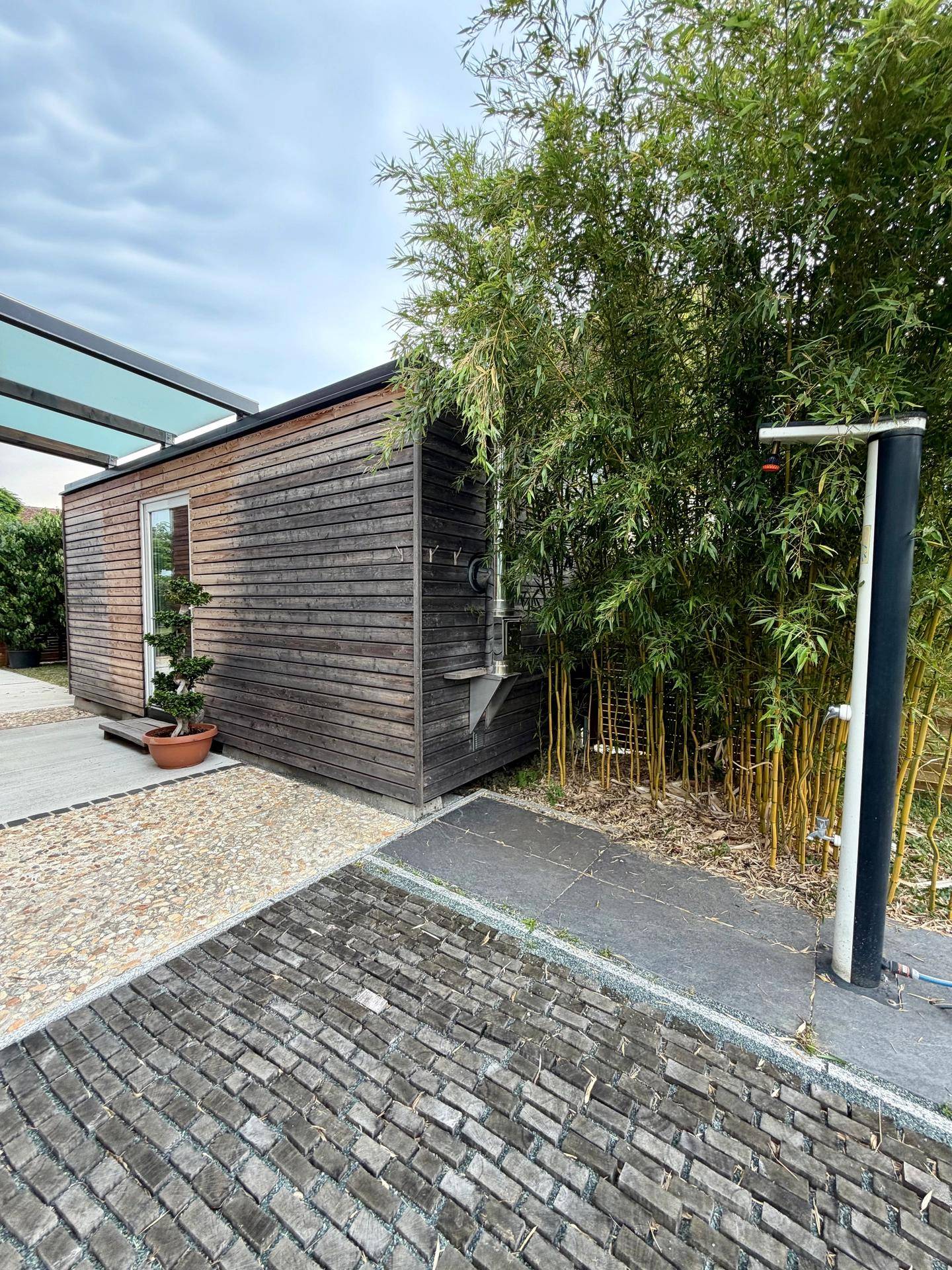 Kleines Holzgebäude im Garten, umgeben von Bambuspflanzen und einem modernen Außenbereich.
