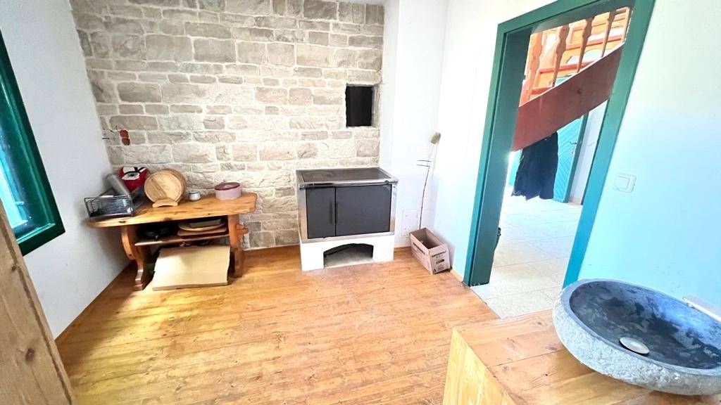 Rustikale Küchenecke mit Steinwand, Holzofen und Holzboden, strahlt traditionellen Charme aus.