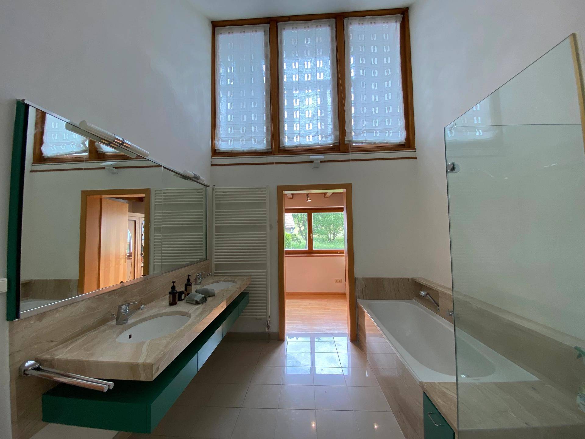 Geräumiges Badezimmer mit Badewanne, Doppelwaschbecken und hohen Fenstern für viel Licht.