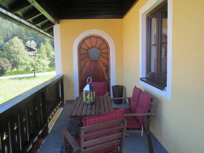Überdachter Balkon mit Holztisch und Stühlen, umgeben von grüner Natur.