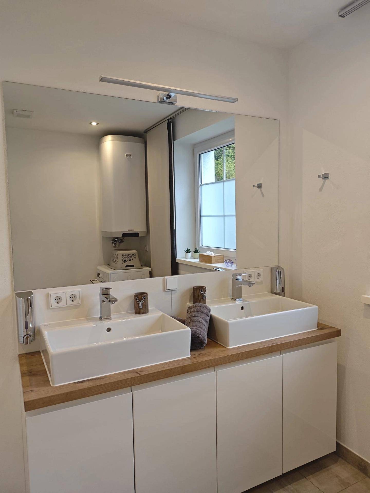 Modernes Badezimmer mit Doppelwaschbecken, großem Spiegel und Fenster für natürliches Licht.