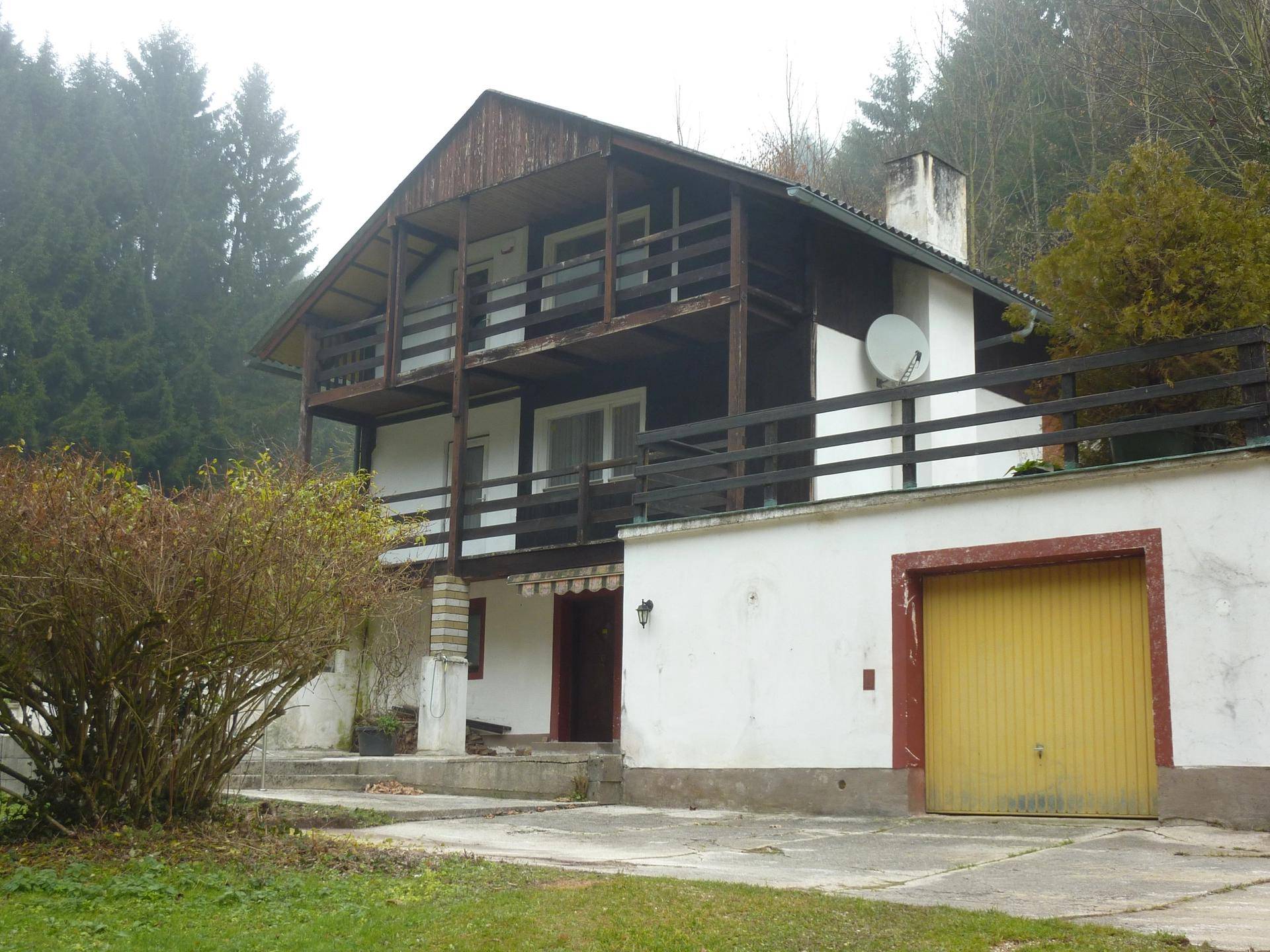 Ansicht des Hauses mit Garage, Balkonen und umgebender Vegetation an einem nebligen Tag.