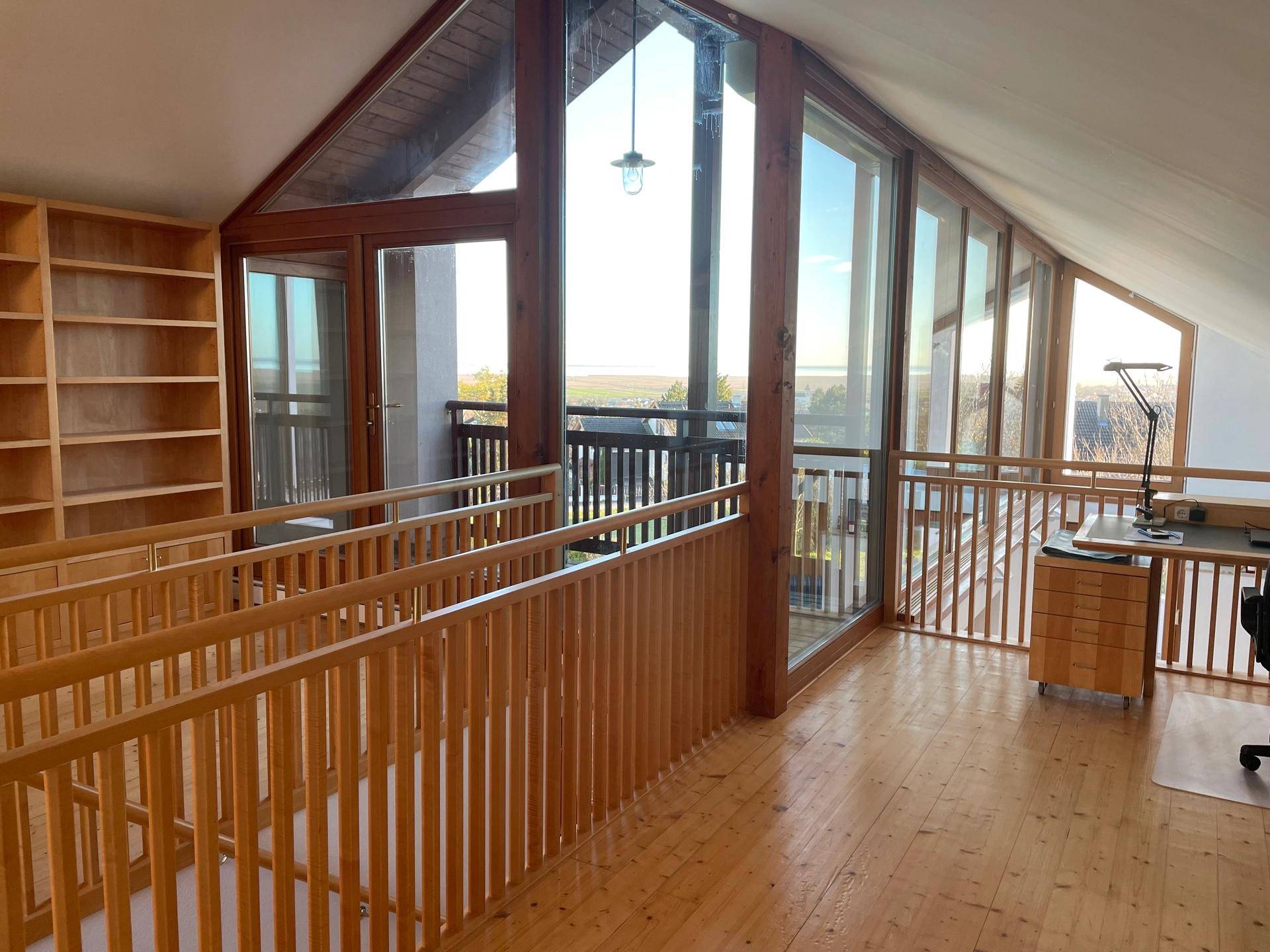 Offener Arbeitsbereich im Obergeschoss mit Holzboden, Einbauregalen und weitem Ausblick durch große Fenster.