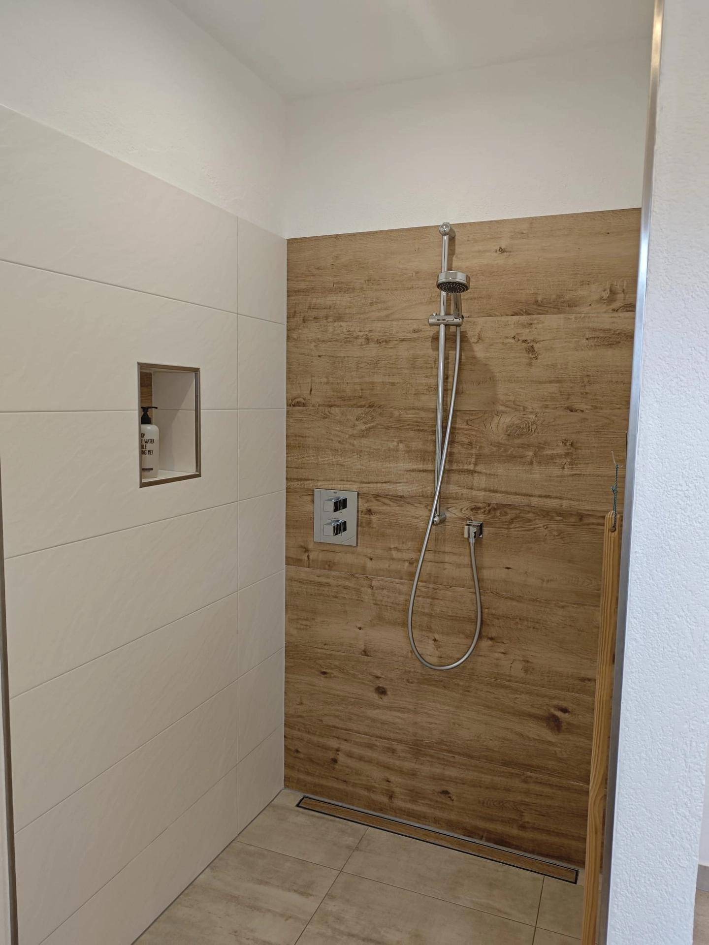 Moderne begehbare Dusche mit Holzwandverkleidung und eleganten Fliesen.