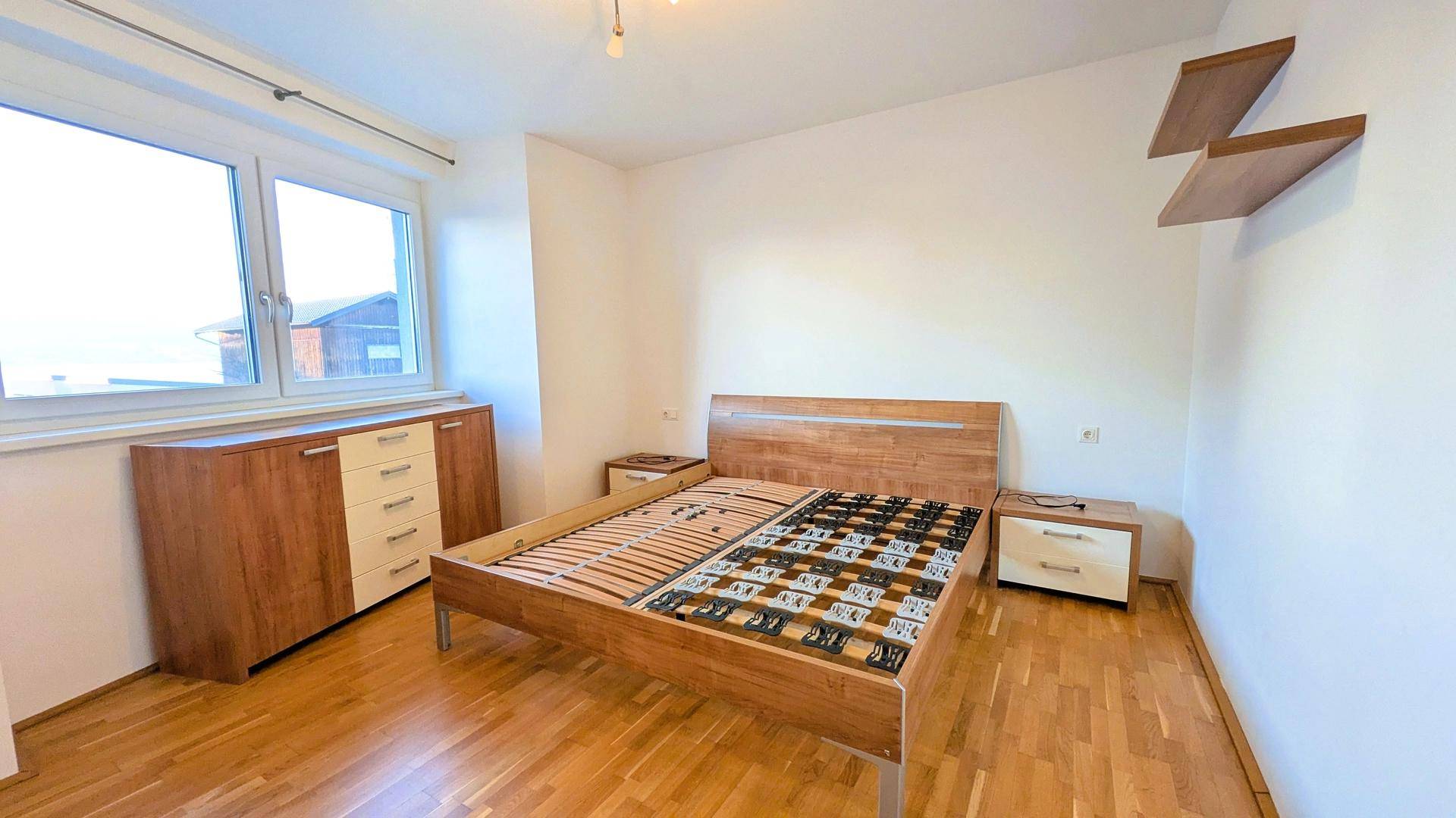 Helles Schlafzimmer mit Holzbettrahmen, Kommode und Fenster, bietet eine ruhige Atmosphäre.