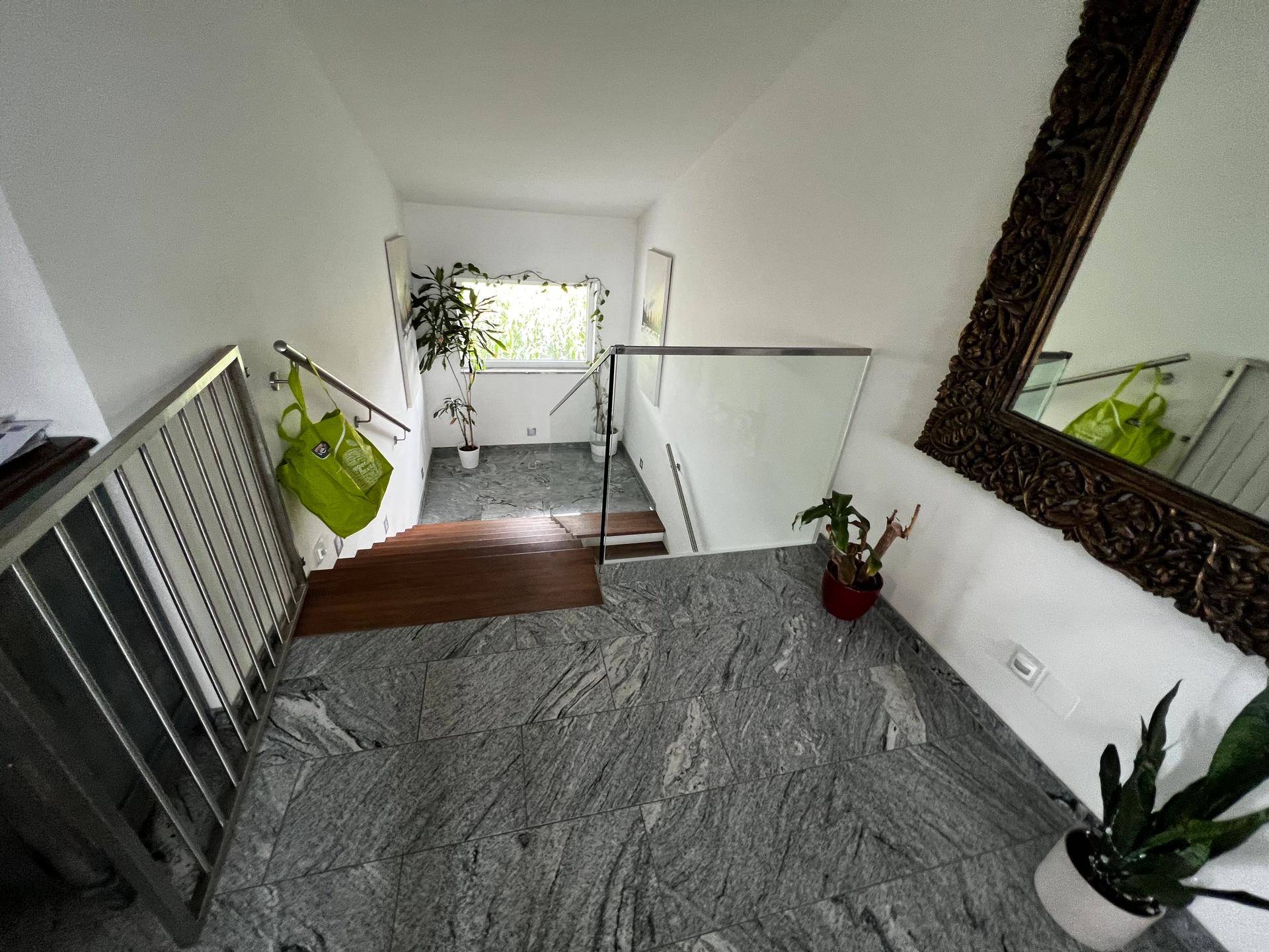 Treppenhaus mit grauem Fliesenboden, modernem Glasgeländer und Pflanzen.
