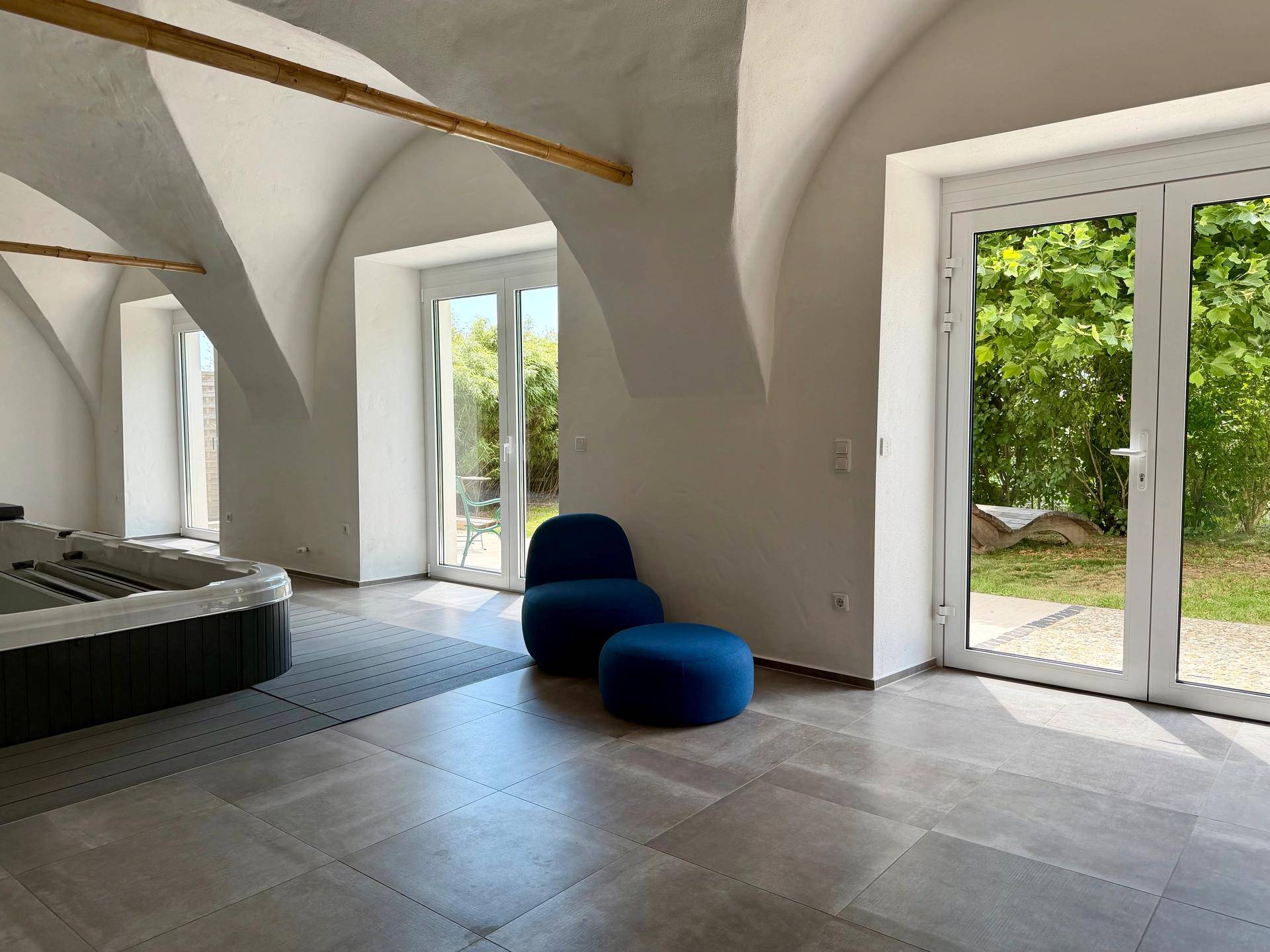 Heller Wellnessbereich mit Whirlpool, Fliesenboden und Zugang zum Garten durch große Türen.