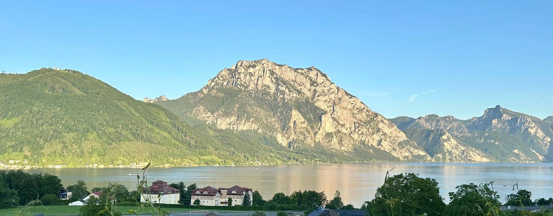 Atemberaubender Panoramablick auf den ruhigen See und die imposanten Berge unter blauem Himmel.