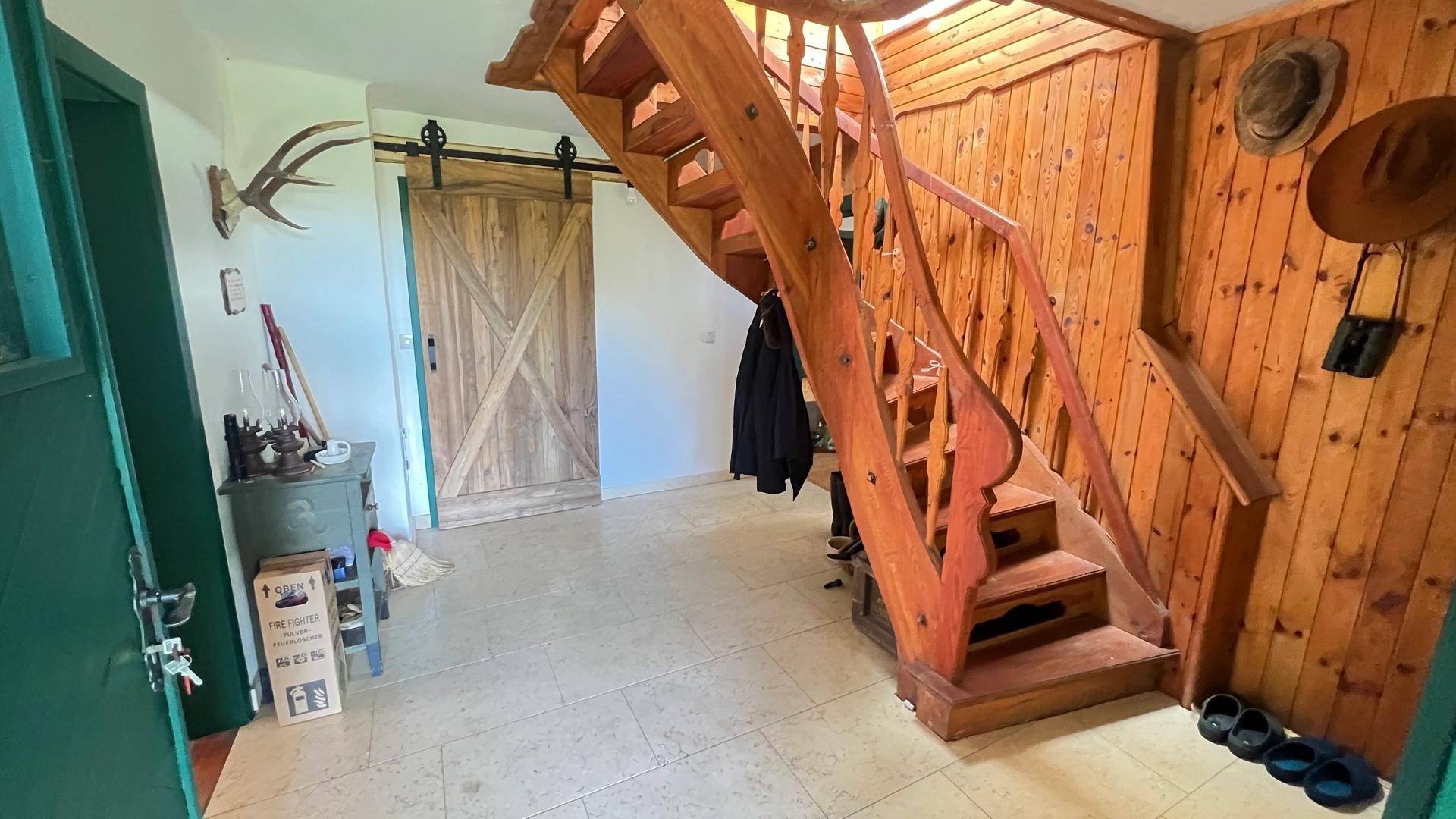 Rustikaler Eingangsbereich mit Holztreppe, Fliesenboden und Holzwänden, dekoriert mit Jagdtrophäen.