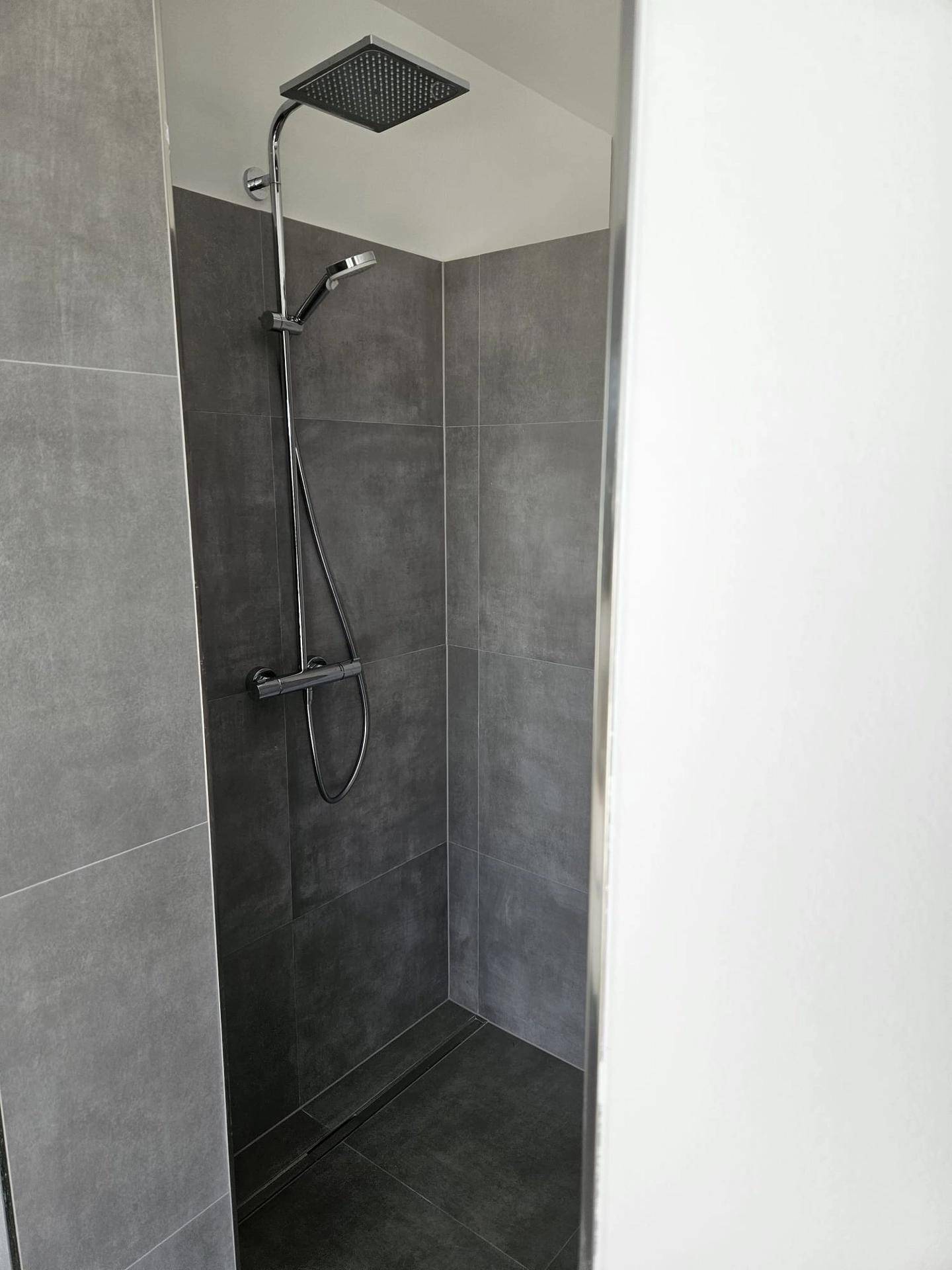 Moderne Duschkabine mit grauen Fliesen und Regenduschkopf, minimalistisch und funktional.