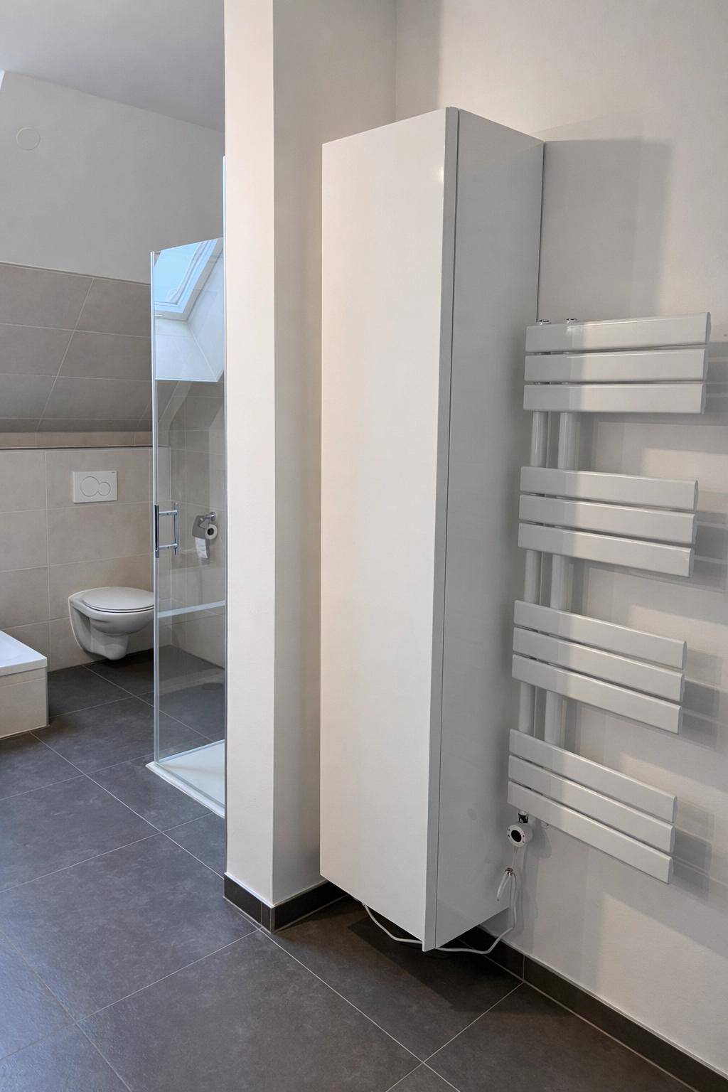 Helles Badezimmer mit modernem Handtuchheizkörper und praktischem Hochschrank für zusätzlichen Stauraum.