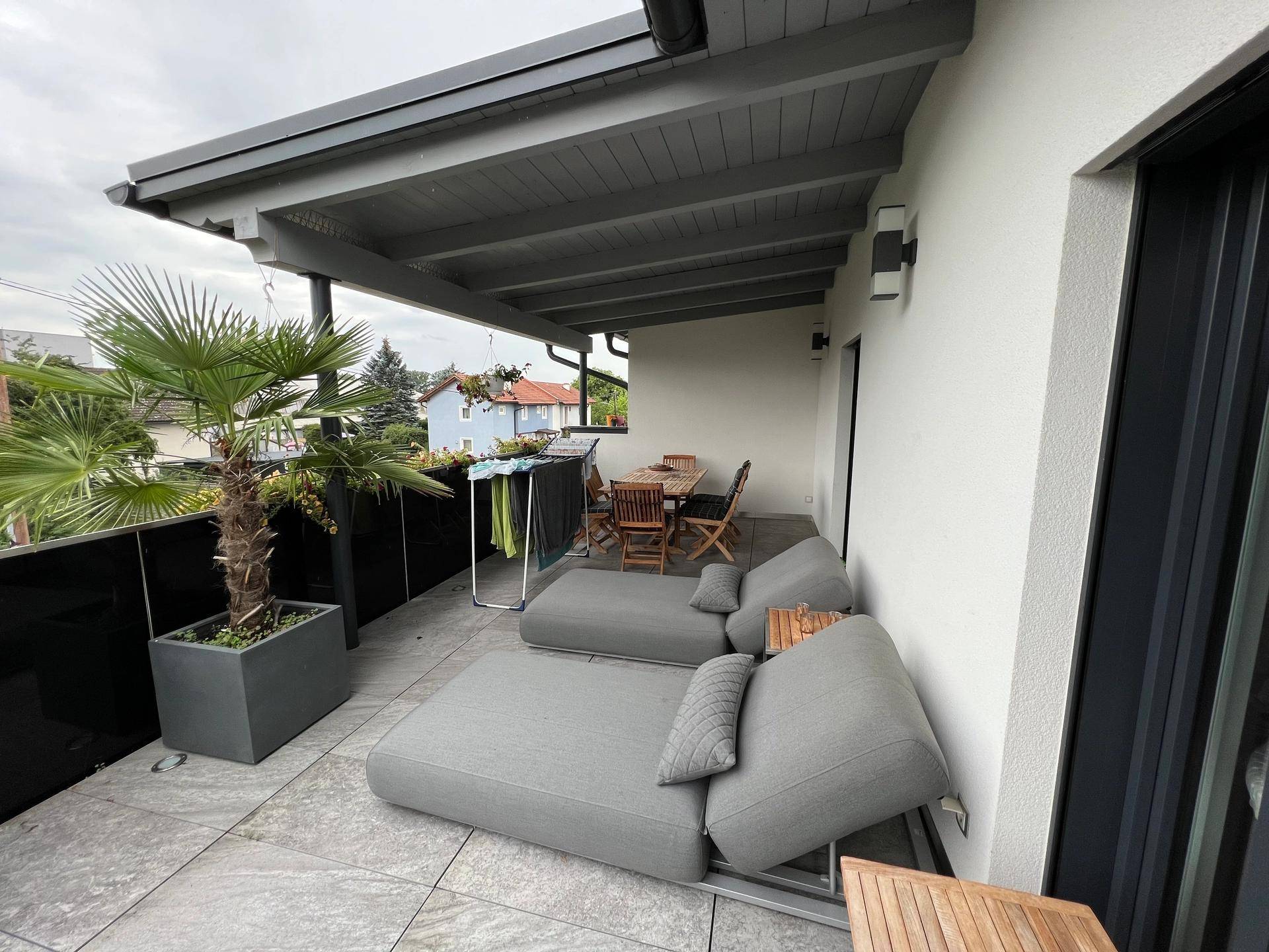 Überdachter Balkon mit bequemen Lounge-Möbeln, Esstisch und Blick ins Grüne.