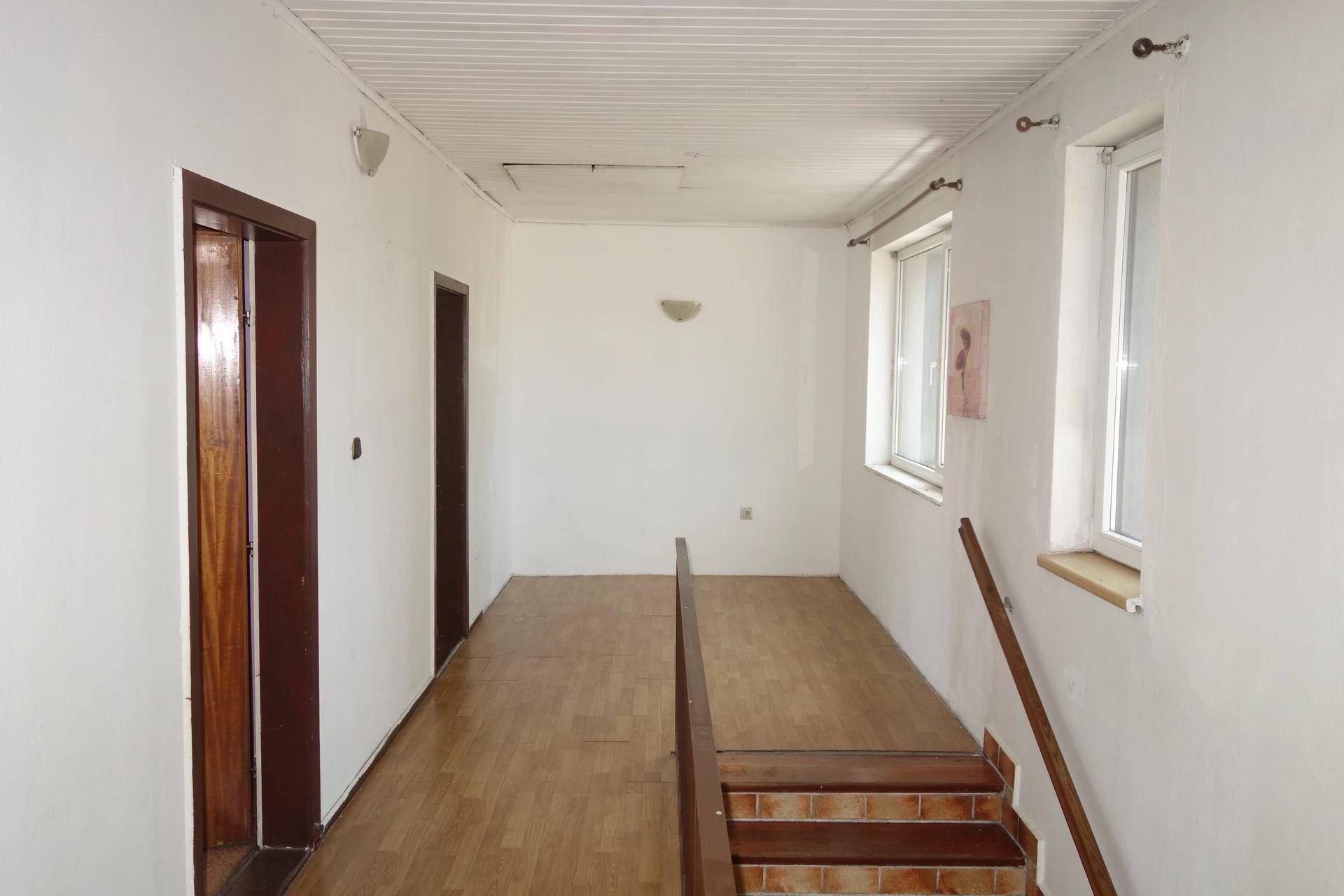 Oberer Flur mit hellem Laminatboden, weißen Wänden, Fenstern und einer Dachschräge.