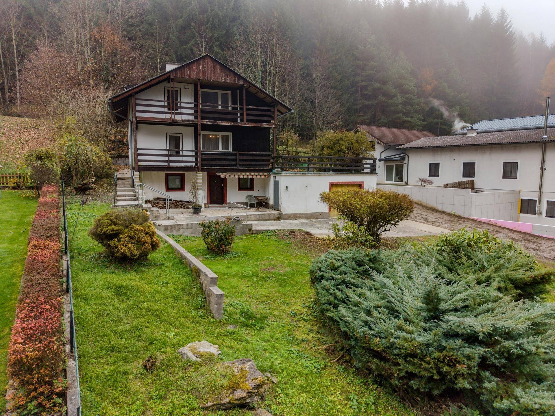Gartenbereich mit Rasenfläche, Sträuchern und Blick auf das Haus und die umliegende Natur.