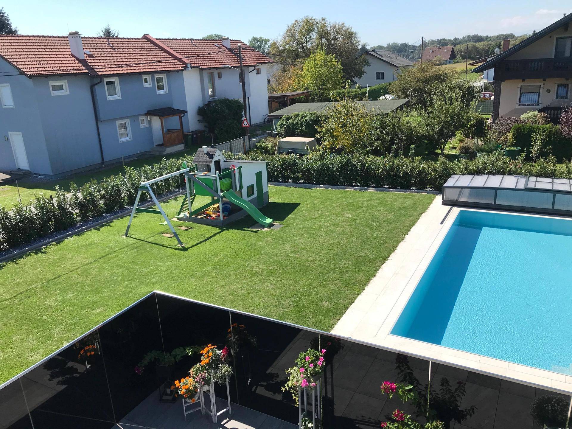 Vogelperspektive auf den weitläufigen Garten mit Pool, Kinderspielplatz und umliegender Hecke.