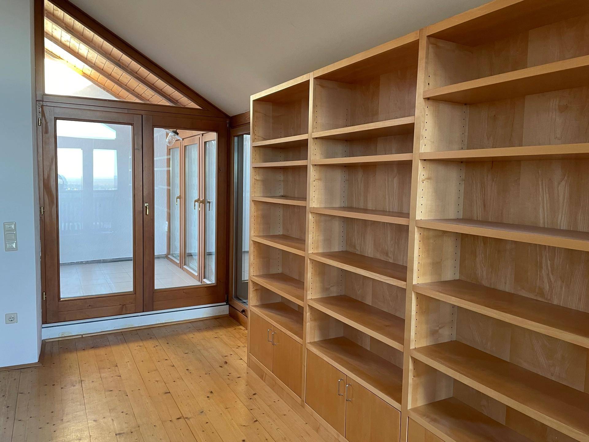 Raum mit großen Einbauregalen aus Holz und Zugang zu einem Balkon durch Glastüren.