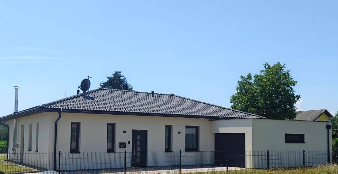 Modernes Einfamilienhaus mit dunklem Ziegeldach und heller Fassade unter blauem Himmel.