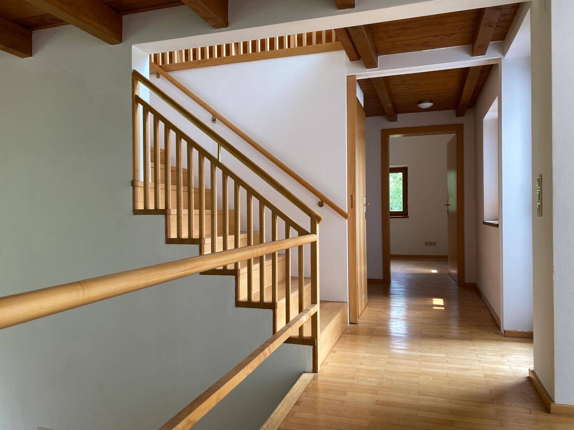 Heller Flur mit Holztreppe und sichtbaren Holzbalken an der Decke, der zu weiteren Räumen führt.