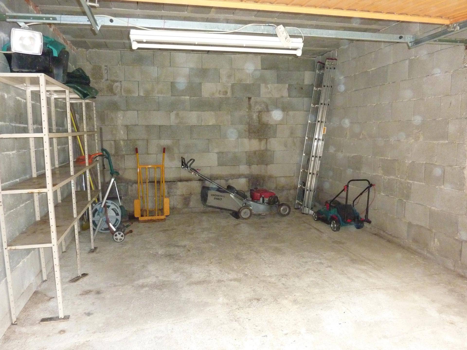 Garage mit Betonwänden, Regalen und Gartengeräten.