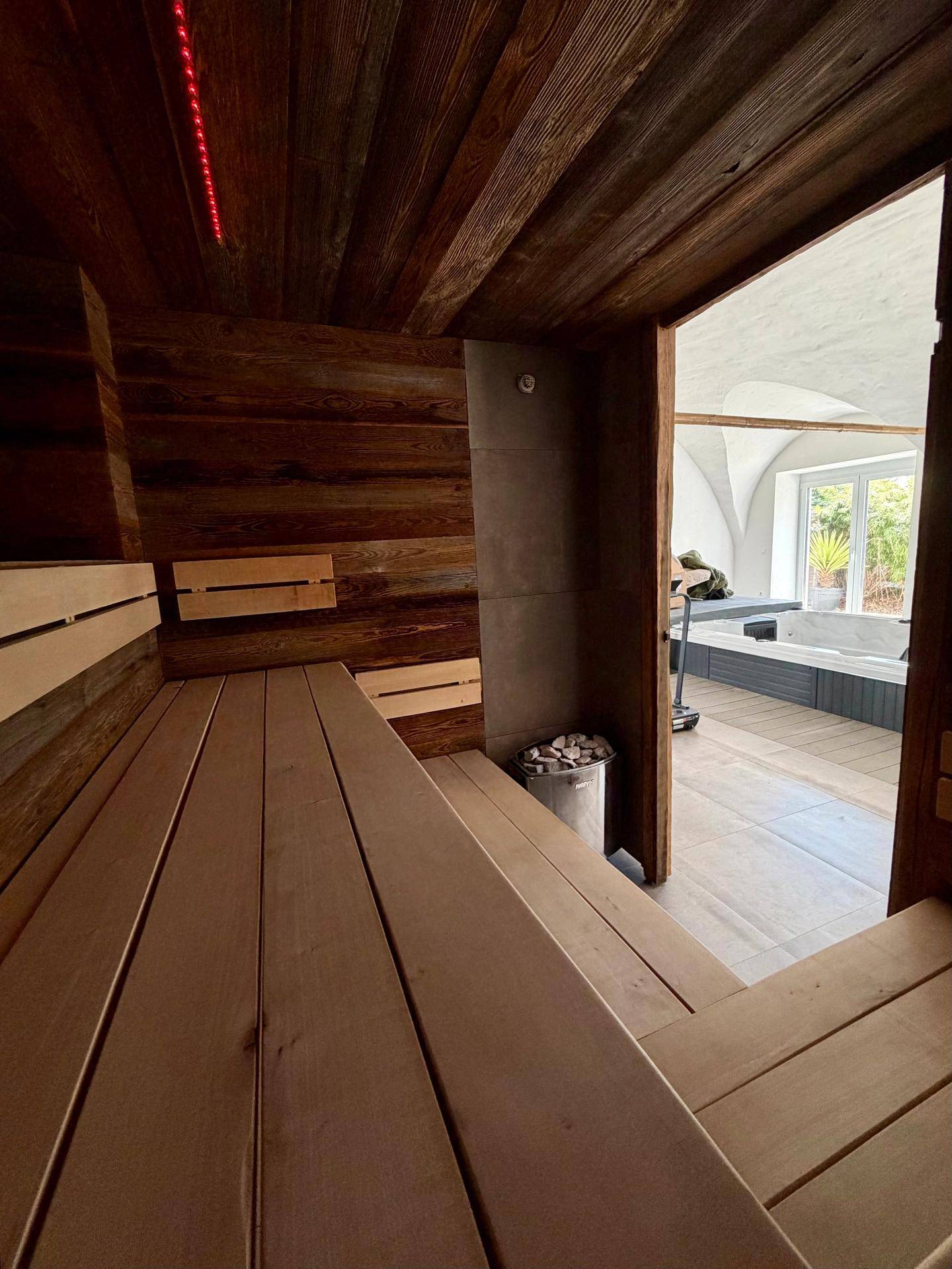 Gemütliche Holzsauna mit Blick auf den Fitnessbereich und einen Whirlpool im Hintergrund.