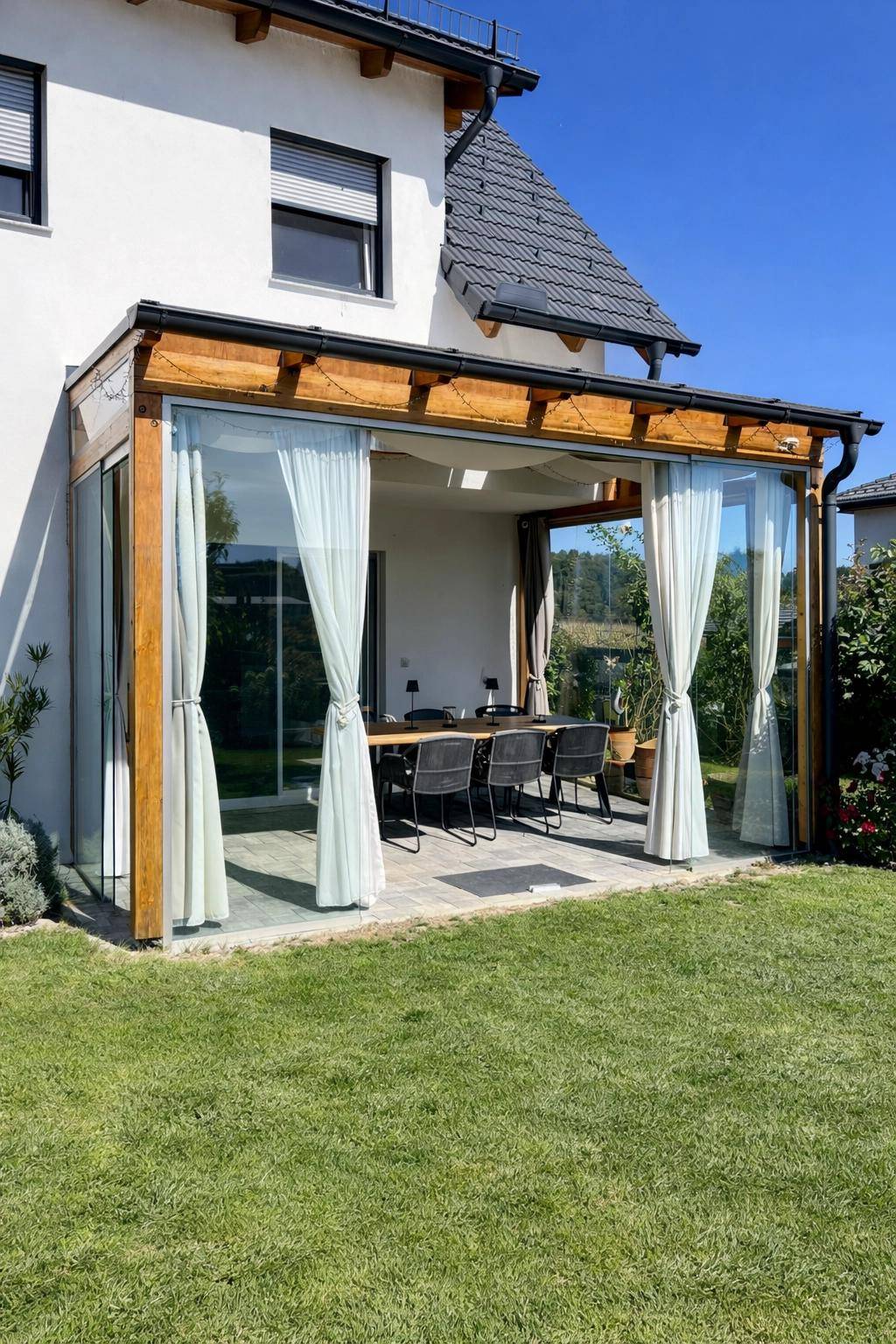 Geräumige, verglaste Terrasse mit großem Esstisch und Blick in den Garten.