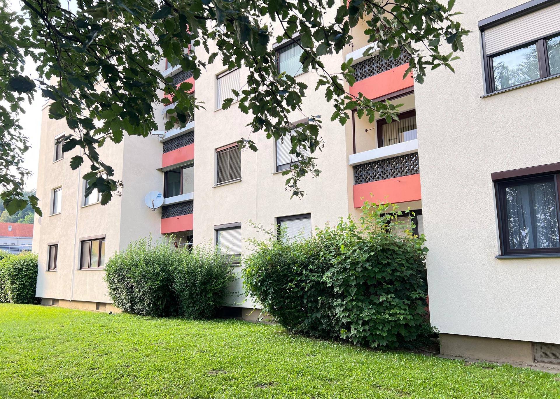 Mehrfamilienhaus mit Balkonen, umgeben von Bäumen und einer Rasenfläche.
