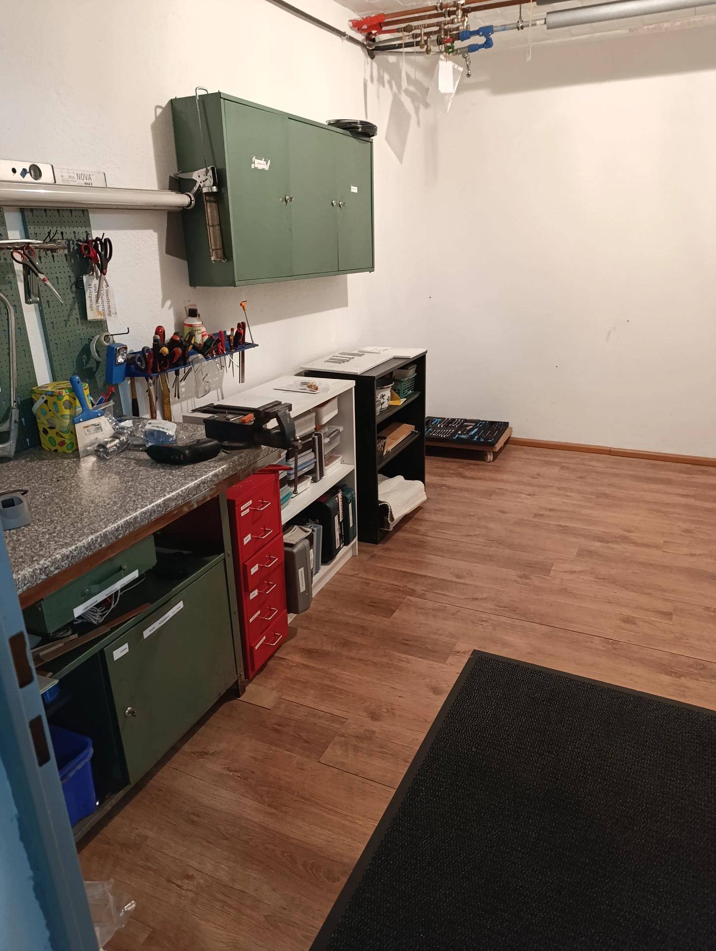 Werkstatt oder Hobbyraum mit Arbeitsplatte, Regalen und Werkzeugen an der Wand.