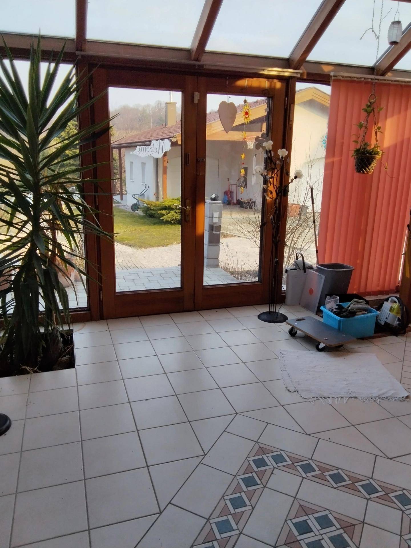 Heller Wintergarten mit Fliesenboden, großen Fenstern und Blick in den Garten.