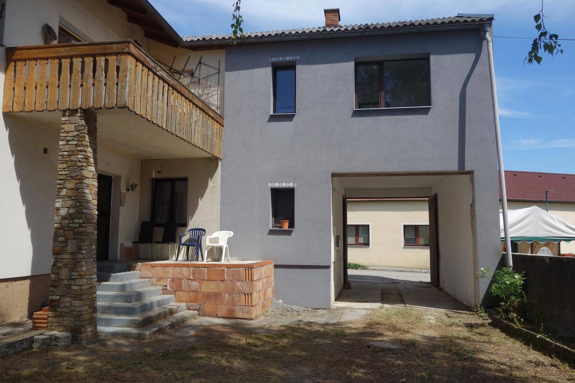 Rückansicht des Gebäudes mit Holzbalkon, einem gemauerten Bereich und einem Durchgang zum Hof.