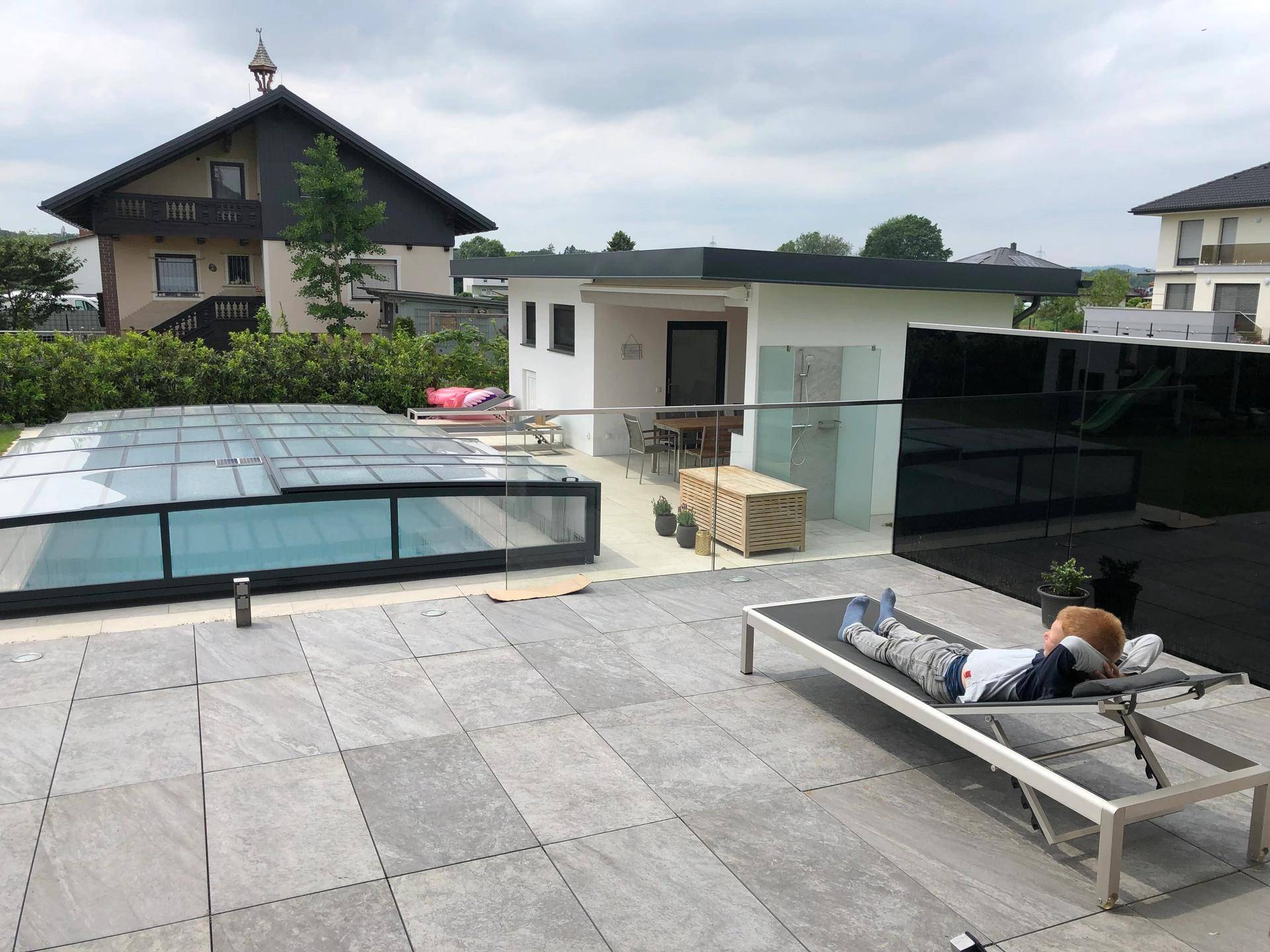 Geräumige Terrasse mit Poolabdeckung, Liegestühlen und einem separaten Gartenhaus im Hintergrund.