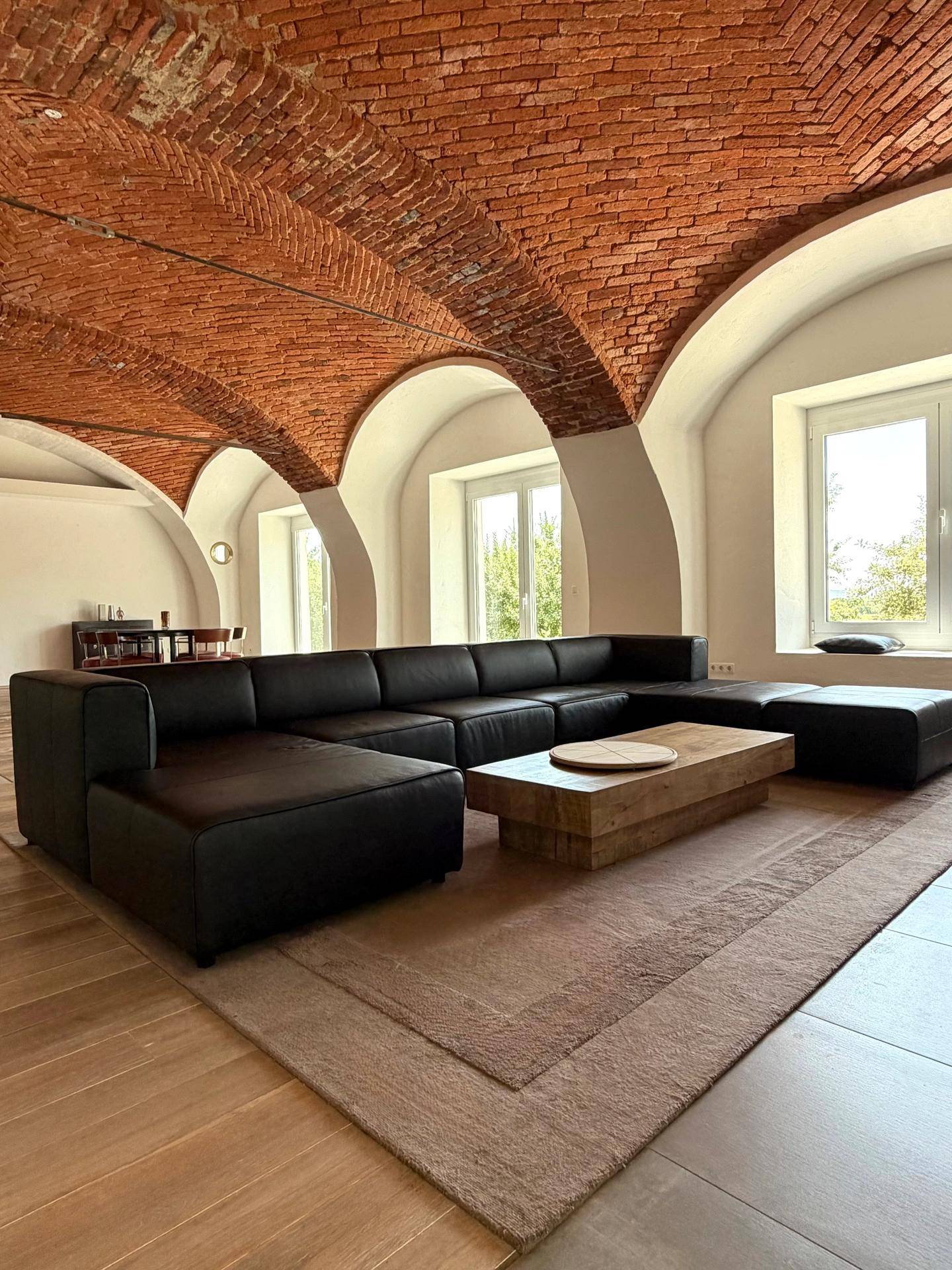Heller Wohnbereich mit großem Ecksofa, Holzboden und beeindruckender Ziegelgewölbedecke.