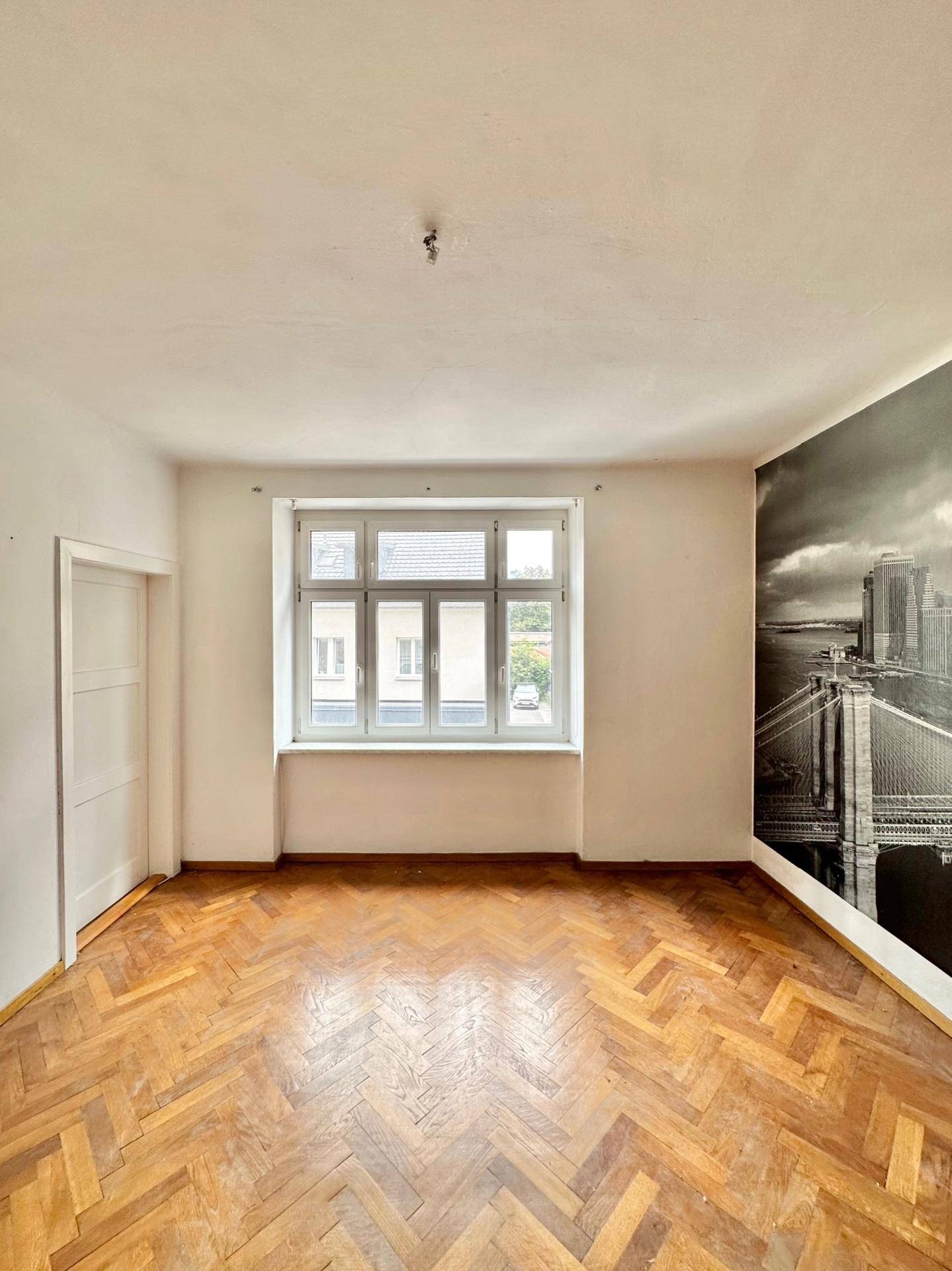 Heller Raum mit Fischgrätparkett und einer Wanddekoration mit Stadtmotiv.